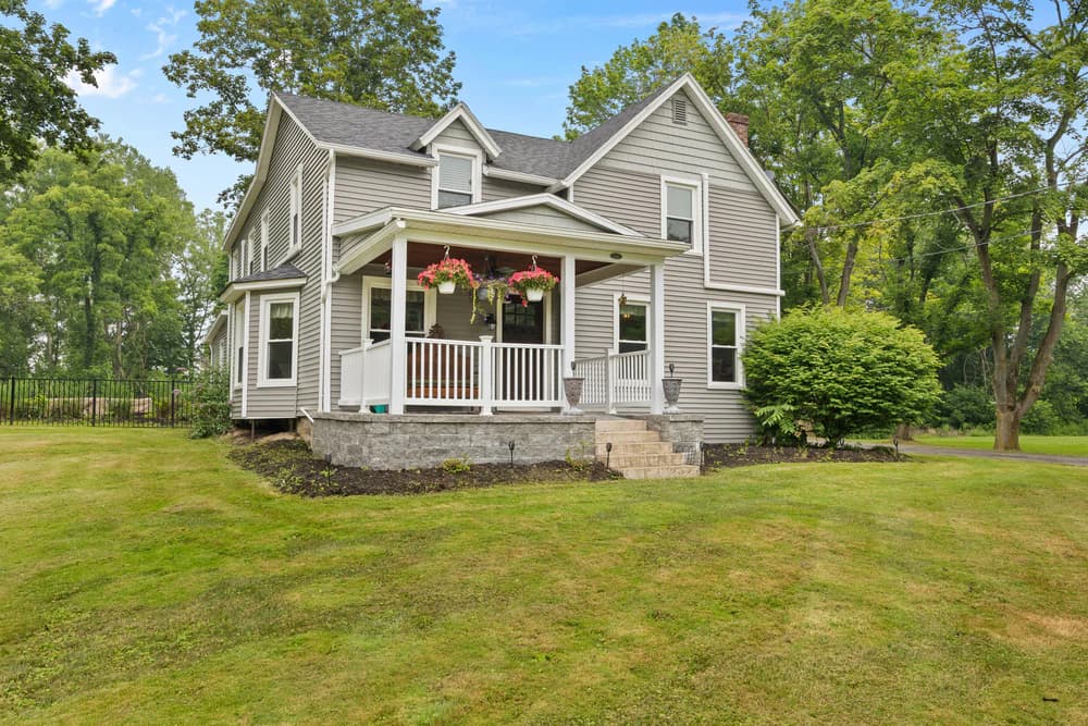 Gray farmhouse with a covered front porch and hanging flower baskets