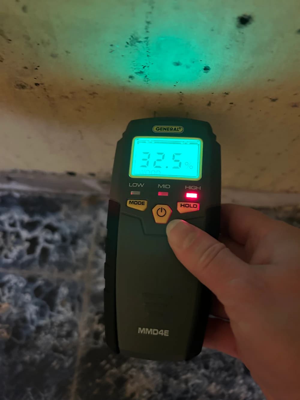 Moisture meter showing a high reading against a damp foundation wall